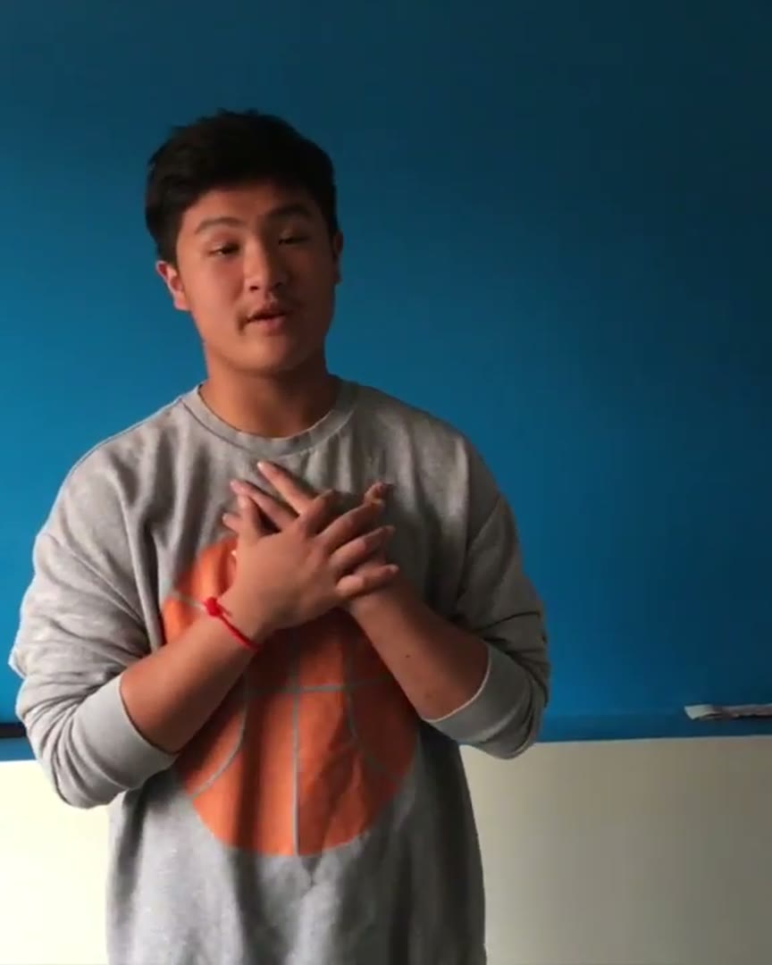 Cameron at 16 in 2016, giving a speech in a grey sweater against a blue wall